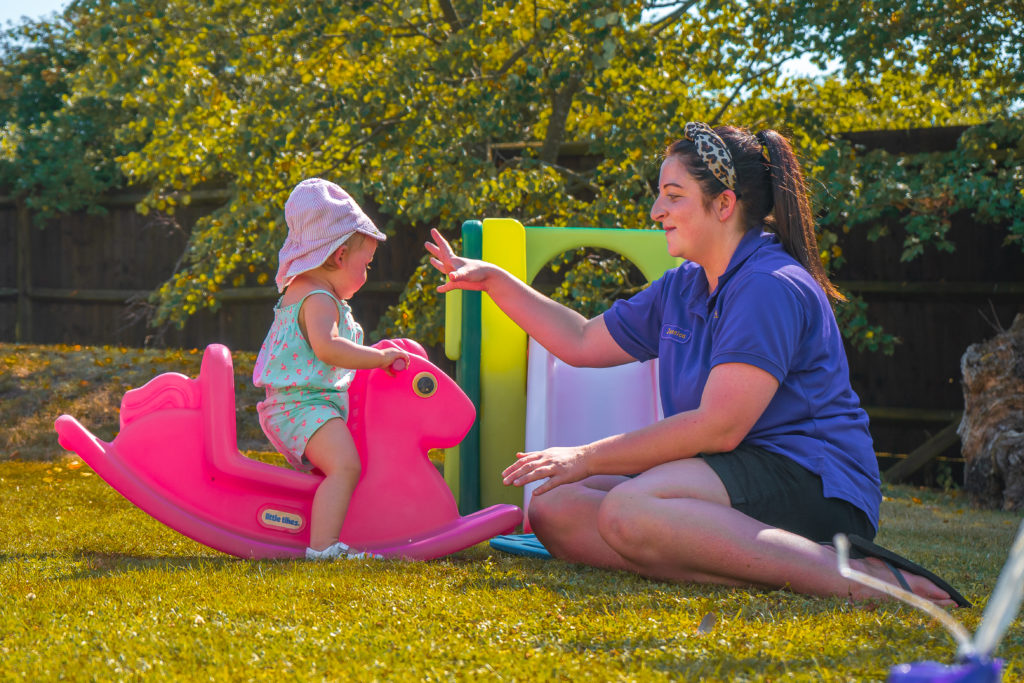 Nursery worker with girl on pink play horse